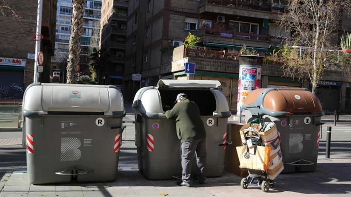 Un hombre recoge un pantalón de los contenedores, en Nou Barris.