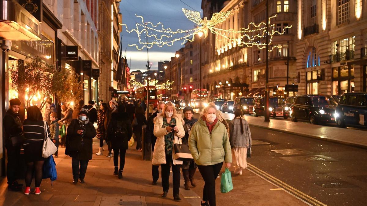 Ciudadanos con mascarilla pasean por una calle comercial de Londres.
