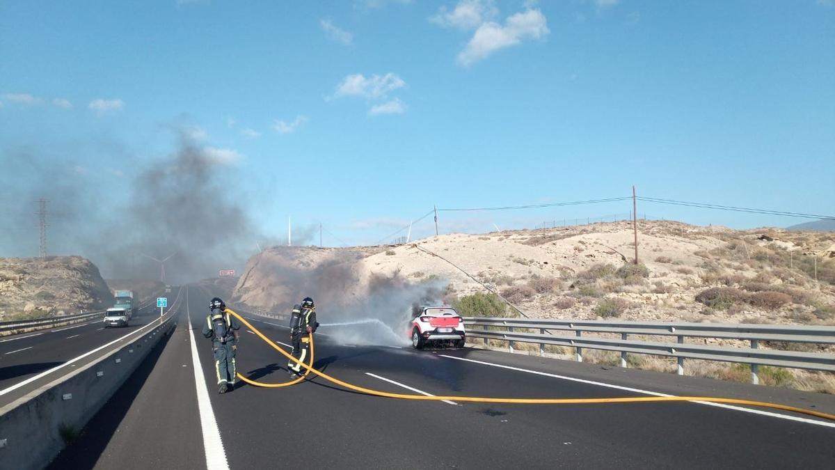 Efectivos de bomberos sofocan las llamas en un coche en plena autopista.