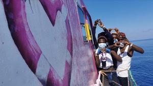 Algunos migrantes junto a la imagen del flotador en forma de corazón en el ’Louise Michel’, el barco de salvamento financiado por de Banksy.