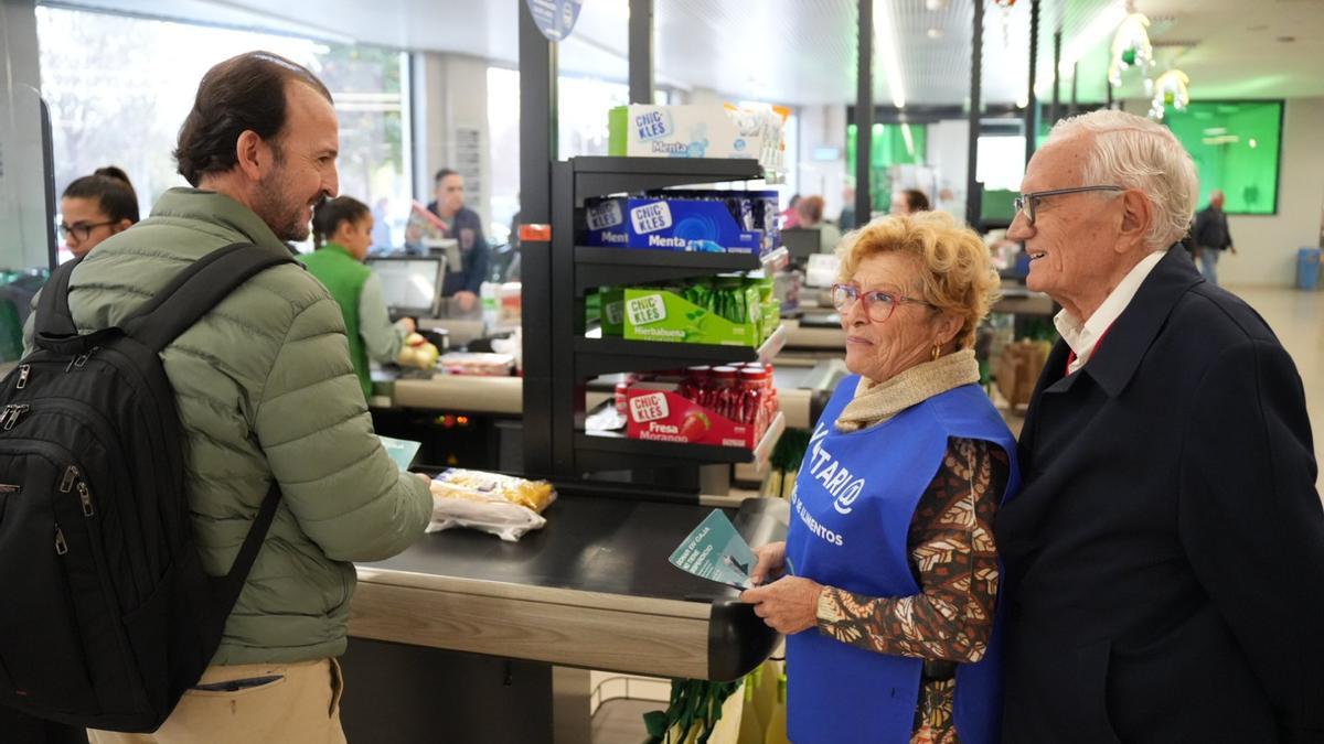 Una voluntaria anima a un cliente a colaborar en la Gran Recogida de Alimentos en una tienda de Mercadona.