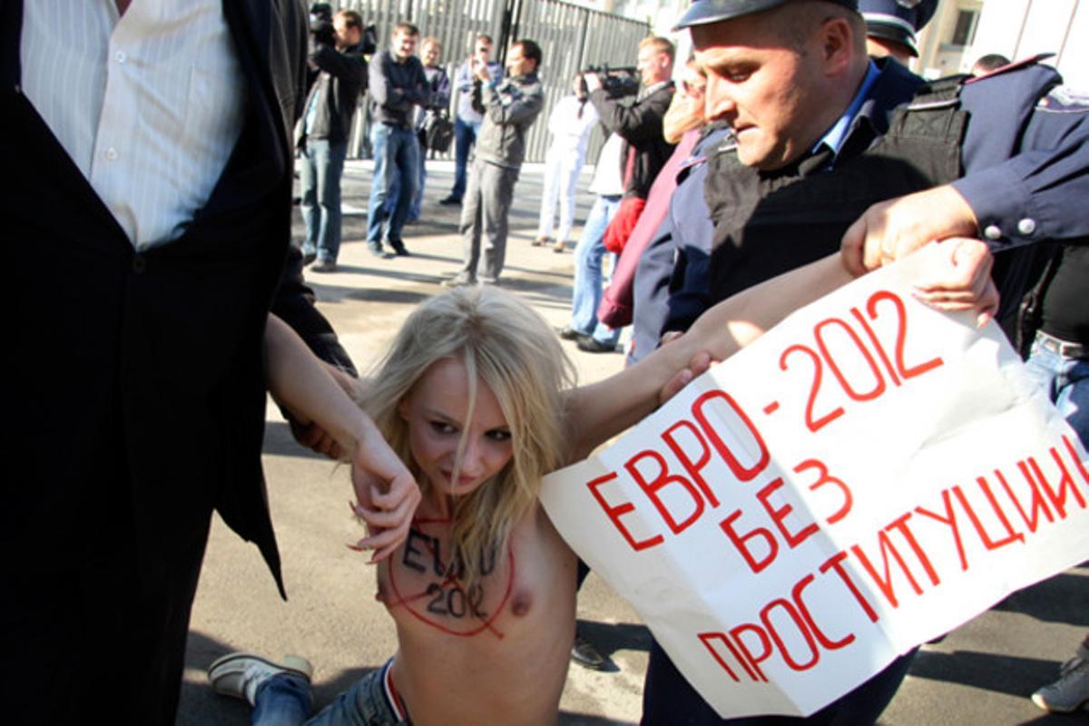 Guàrdies de seguretat detenen una activista que denuncia el turisme sexual i la prostitució a Ucraïna. Al cartell hi diu: Euro 2012 sense prostitució, en referència al campionat de futbol de l’any que ve.