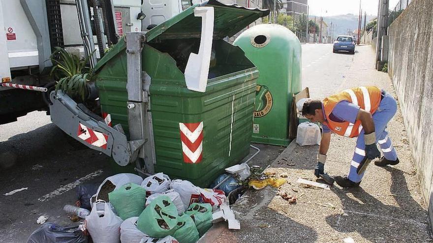 Un trabajador del servicio de recogida de basura limpia el entorno de un contenedor.  // Santos Álvarez