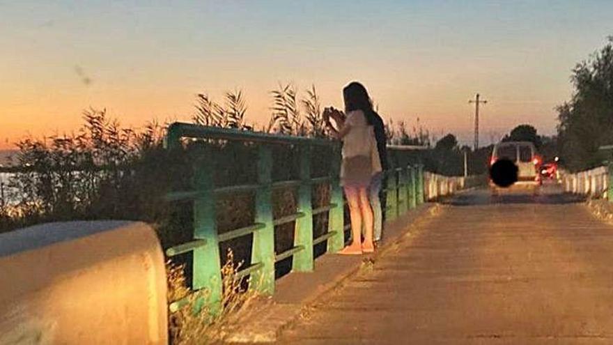 Dos jóvenes asomadas al puente del Palmar haciendo una foto del atardecer sobre el lago.