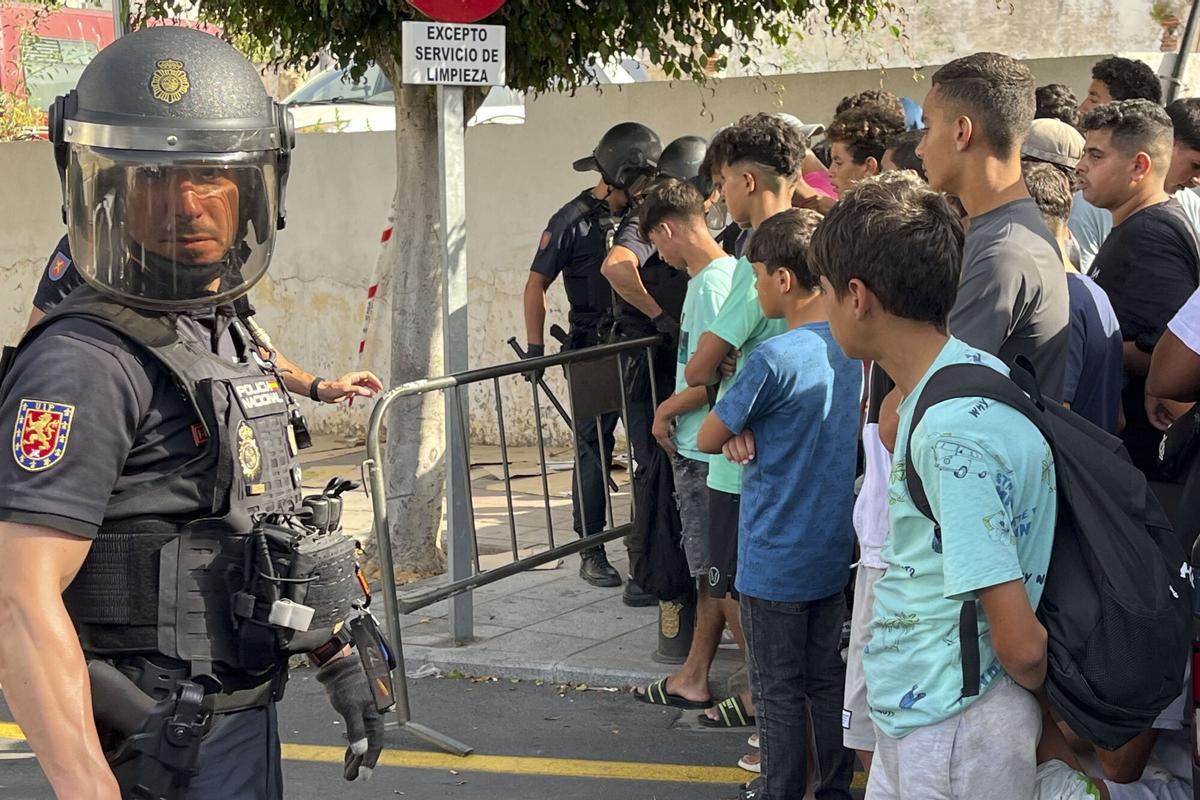 Un policía nacional custodia a multitud de menores migrantes que esperan para su filiación.