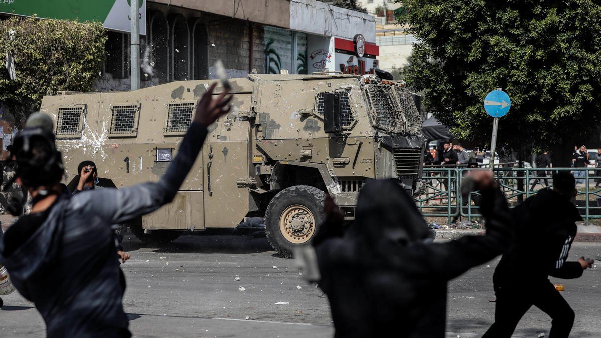 Un grupo de palestinos lanzan piedras contra un vehículo militar de Israel durante los enfrentamientos en la ciudad cisjordana de Nablús por una redada del Ejército israelí