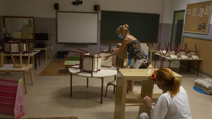 Dos personas desinfectan un aula de un colegio.