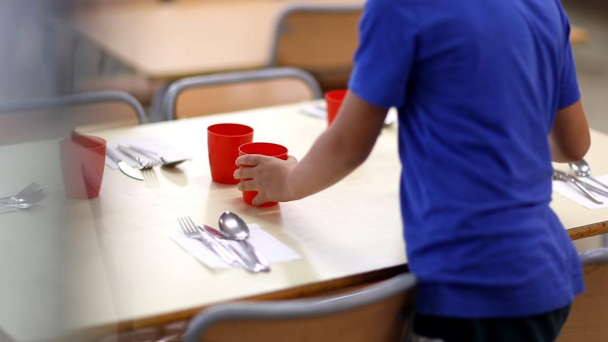 Una mujer coloca una mesa en un comedor escolar.