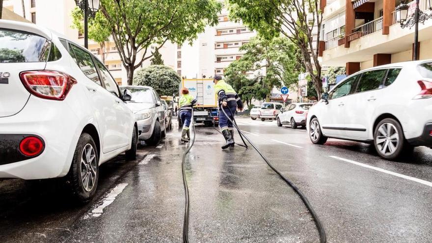 Dos operarios baldean una calle en la zona de Molino de Viento.