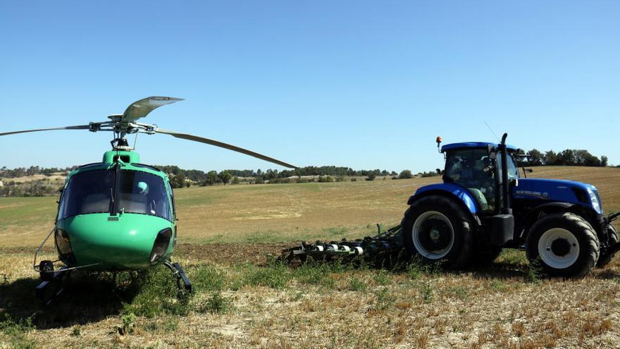 Un tractor llaura al costat d&#039;un helicòpter dels Agents Rurals