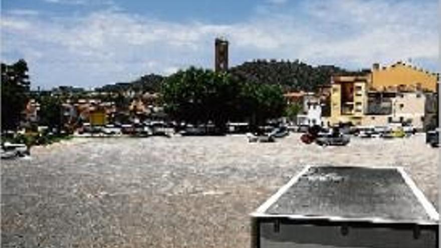 Vehicles estacionats al descampat, amb la plaça i l&#039;església al fons