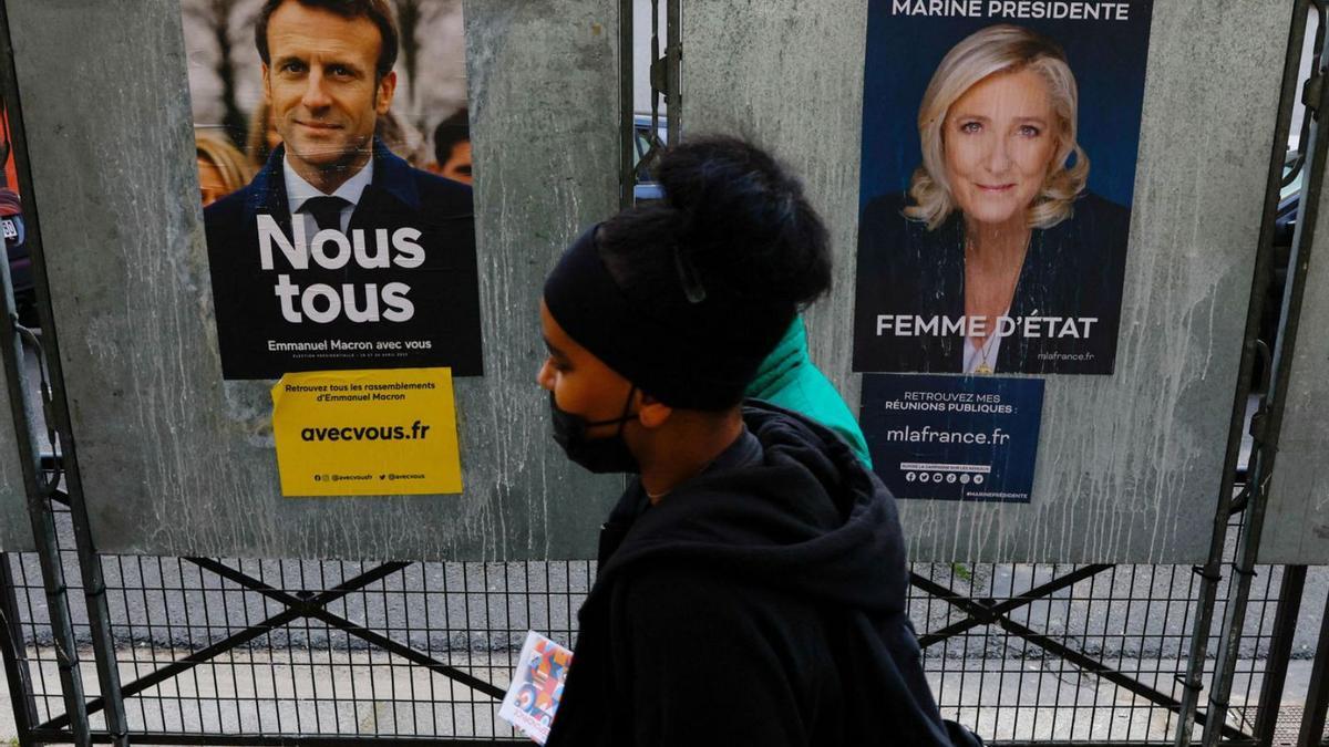 Dues persones passen per davant de cartells electorals de Macron i Le Pen. | GONZALO FUENTES/REUTERS