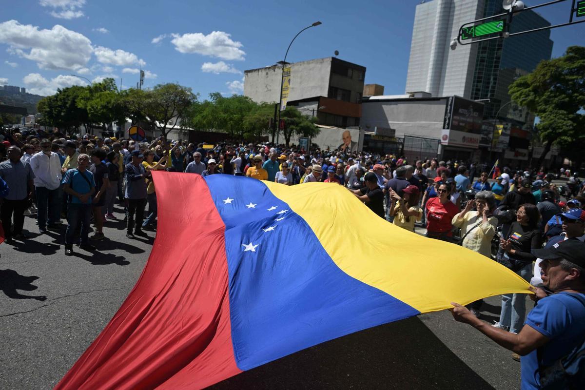 Demonstrators unfold a huge Venezuelan flag during a protest called by the opposition on the eve of the presidential inauguration in Caracas on January 9, 2025. Venezuela is on tenterhooks facing demonstrations called by both the opposition and government supporters a day before President Nicolas Maduro is due to be sworn in for a third consecutive term and despite multiple countries recognizing opposition rival Edmundo Gonzalez Urrutia as the legitimate president-elect following elections past July. (Photo by JUAN BARRETO / AFP)
