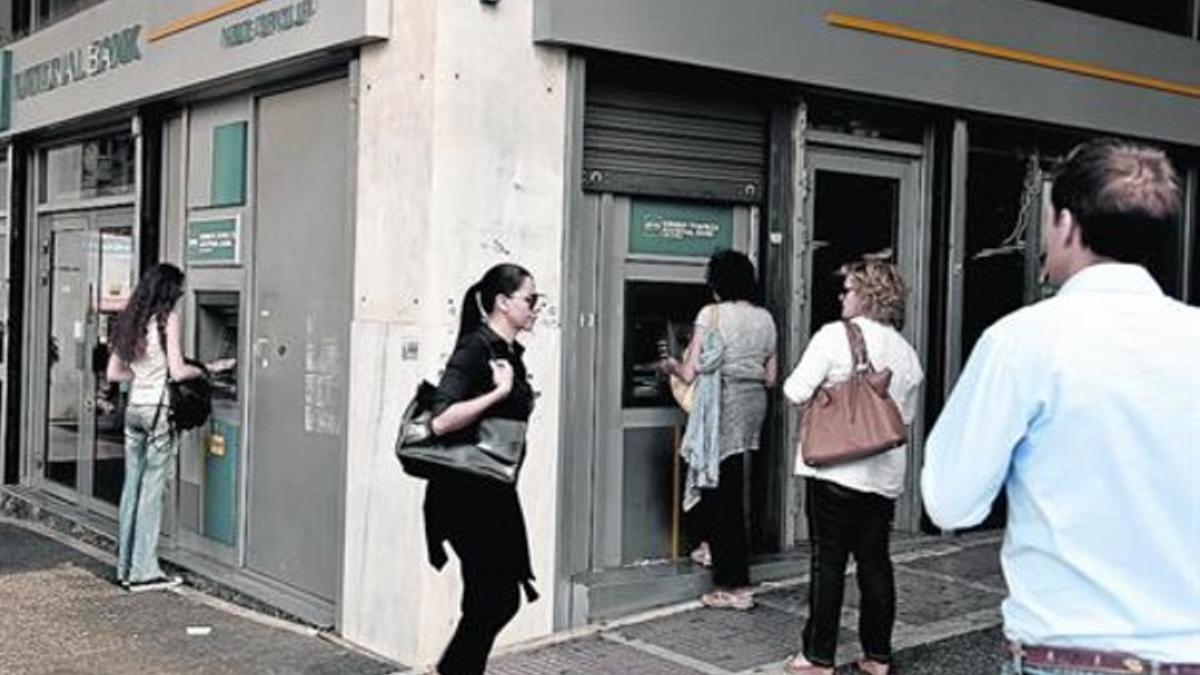 Retirando euros 8 Unos ciudadanos griegos esperan su turno para sacar dinero del cajero, ayer.