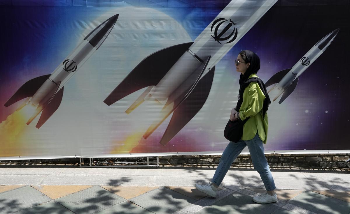 A woman walks past a banner showing missiles being launched, in northern Tehran, Iran, Friday, April 19, 2024. Iran fired air defenses at a major air base and a nuclear site near the central city of Isfahan after spotting drones early Friday morning, raising fears of a possible Israeli strike in retaliation for Tehrans unprecedented drone-and-missile assault on the country. On the missiles, a decorative sign reads: Allah (AP Photo/Vahid Salemi)