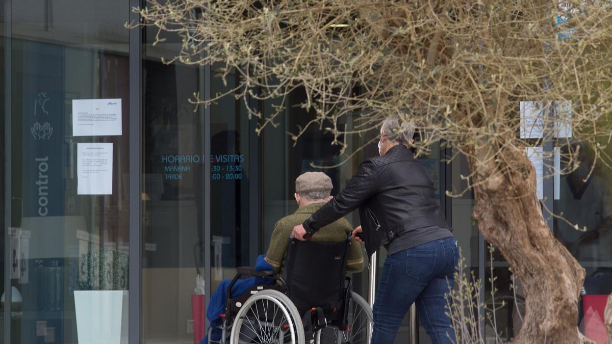 Una mujer pasea a un anciano en una silla de ruedas.