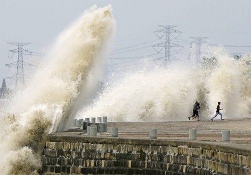 People run away from waves caused by a tidal bore which surged past a barrier on the banks of Qiantang River, in Haining