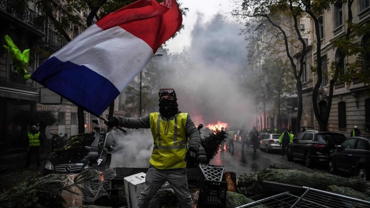 Un 'chaleco amarillo' ondea una bandera francesa durante una protesta en París.