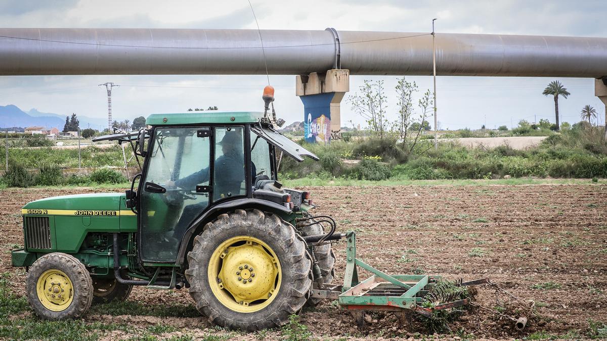 Un agricultor labrando el campo con su tractor junto a tuberías del trasvase