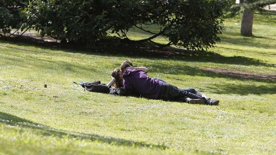 Una pareja se besa en unos jardines.