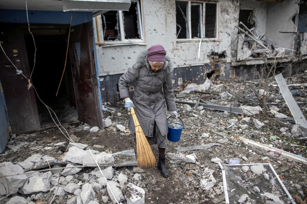Una mujer sostiene una escoba afuera de un bloque de apartamentos gravemente dañado, luego de un ataque de artillería, en medio del ataque de Rusia contra Ucrania, en Kharkiv, Ucrania.