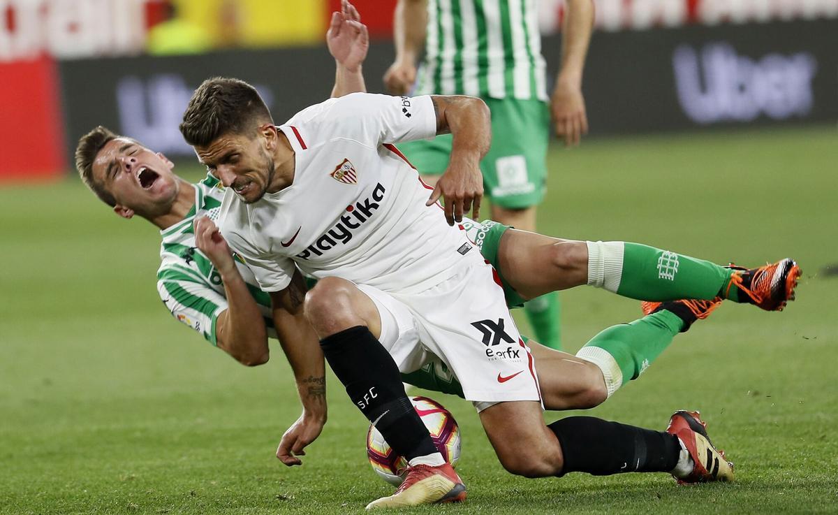GRAF983. SEVILLA, 13/04/2019.- El delantero argentino del Real Betis Giovani Lo Celso (i) cae tras la entrada del portugués Daniel Carriço, del Sevilla FC, durante el partido de la trigésima segunda jornada de Liga en Primera División que Sevilla FC y Real Betis disputan esta noche en el estadio Sánchez-Pizjuán, en Sevilla. EFE/Jose Manuel Vidal.