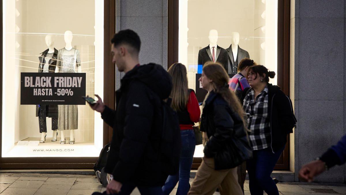 Varias personas pasan por delante de los comercios que anuncian los descuentos del Black Friday.