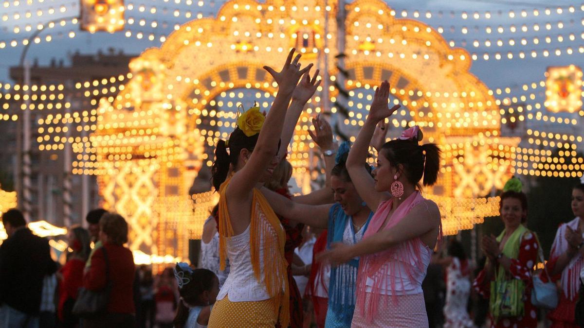 Mujeres bailando sevillanas con la portada de la Feria de Abril al fondo. / El Correo