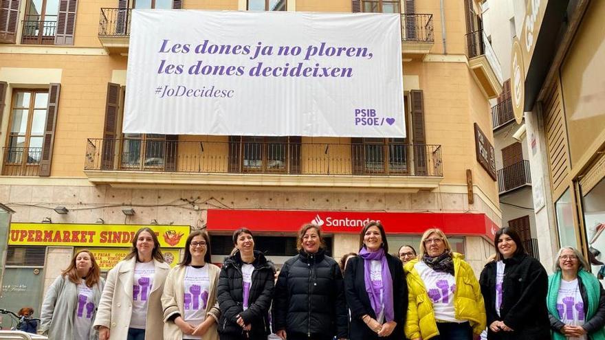 Las líderes del PSIB, ante la lona con el mensaje.