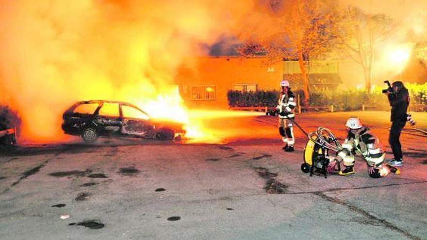 Los bomberos sofocan las llamas de un vehículo incendiado en los disturbios.  // Reuters