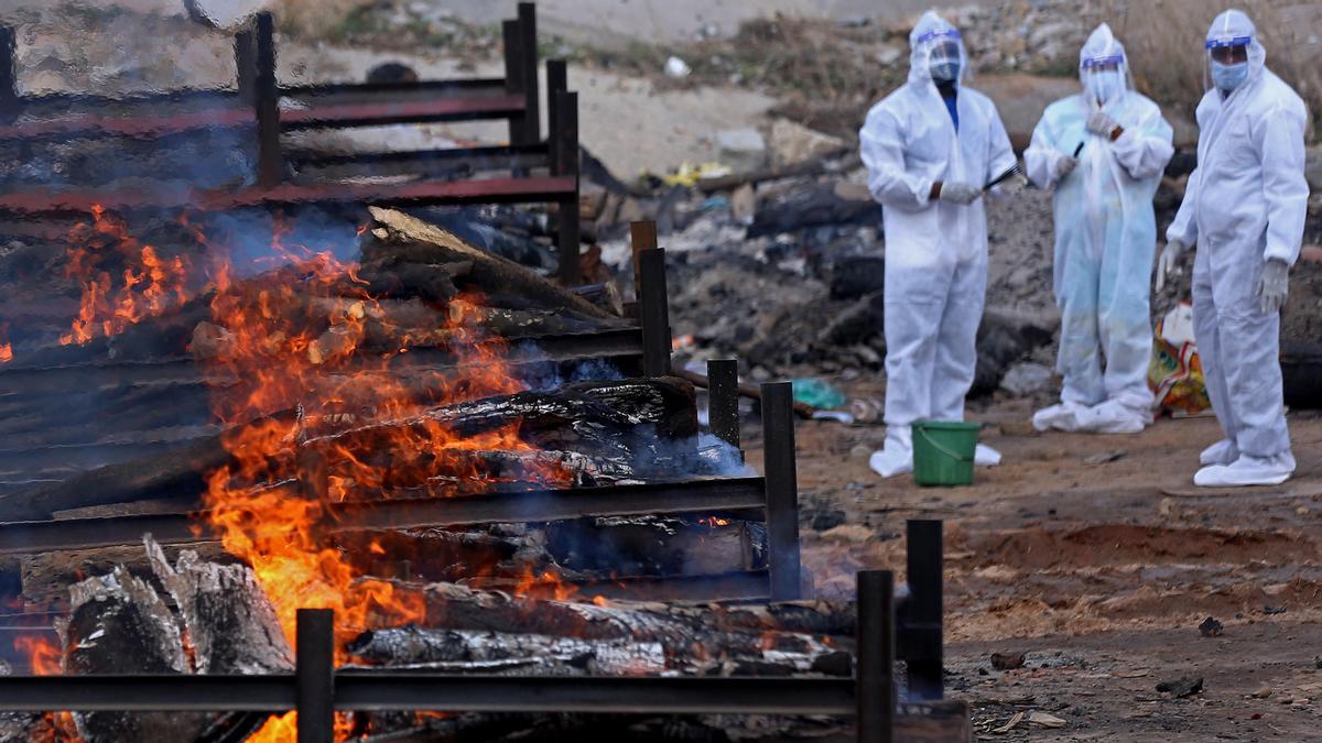 Trabajadores observan una hilera de piras funerarias en India