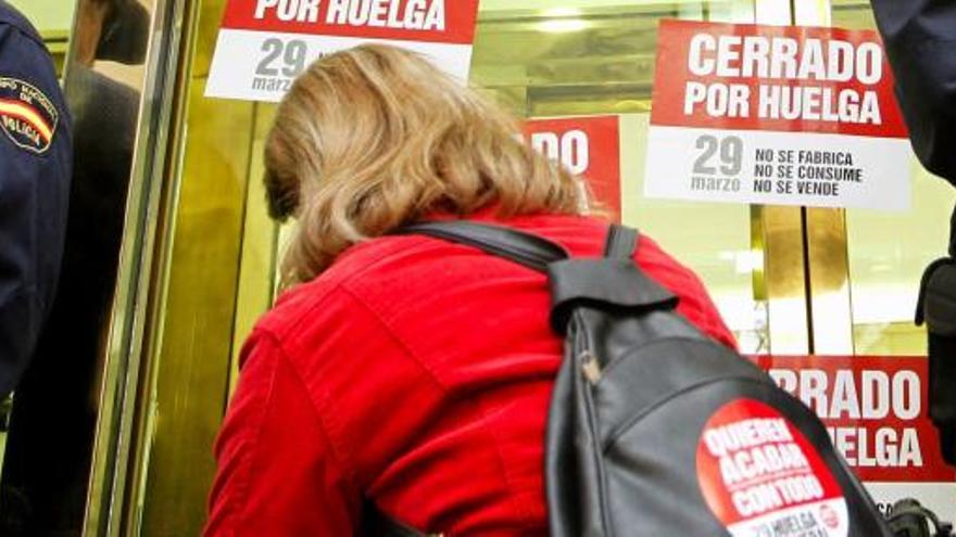 Una mujer de un piquete informativo coloca carteles en un comercio entre dos policías en el centro de Valencia.