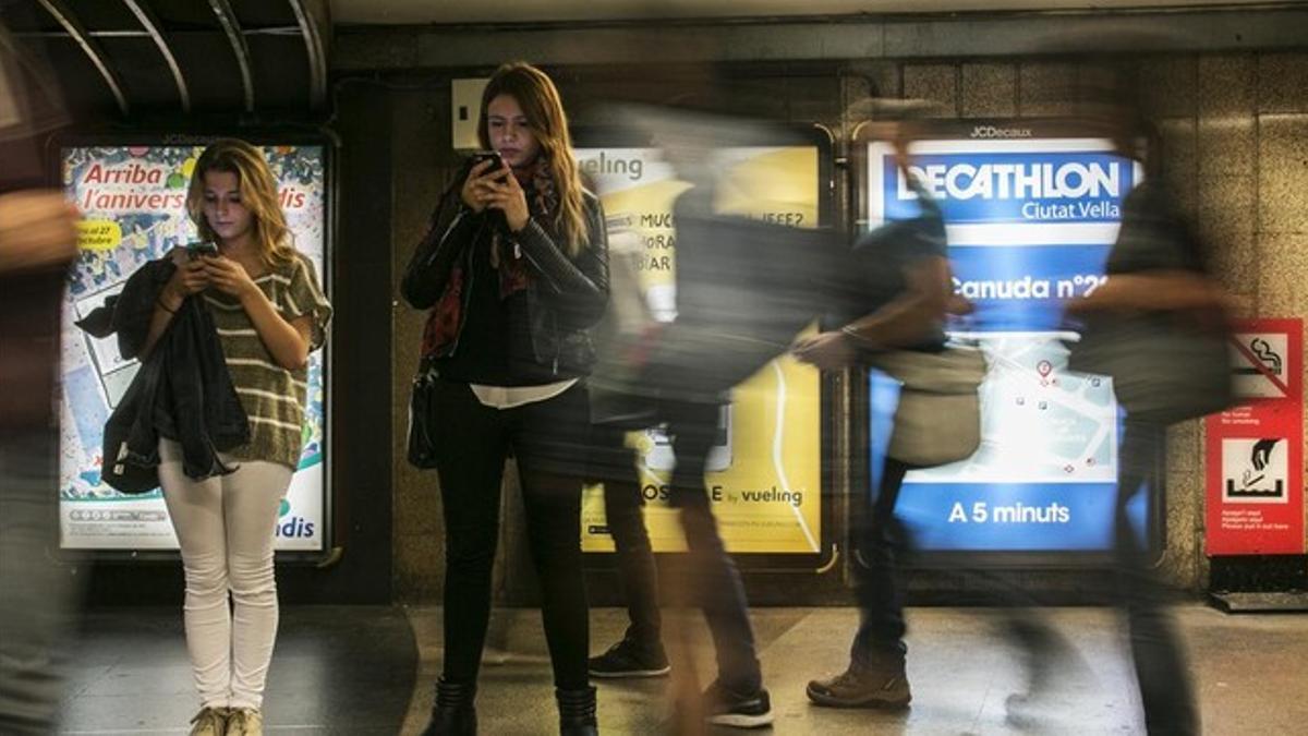 Unas jóvenes miran su móvil en un andén del metro.