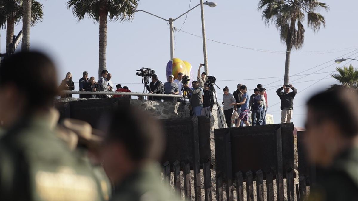 Migrantes en Tijuana, México, miran desde el otro lado del muro durante una visita de la Secretaria de Seguridad, Kirjsten Nielsen.