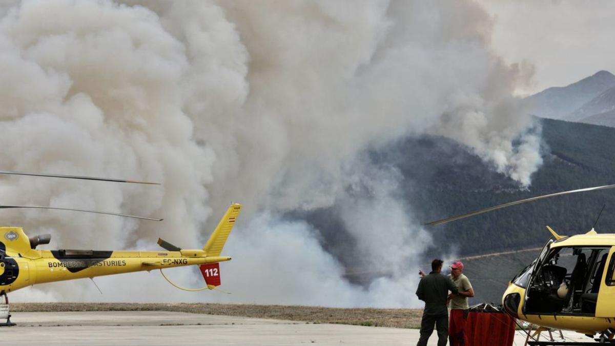 Dos de los helicópteros que participan en las tareas de extinción, con la gran humareda del fuego detrás. |