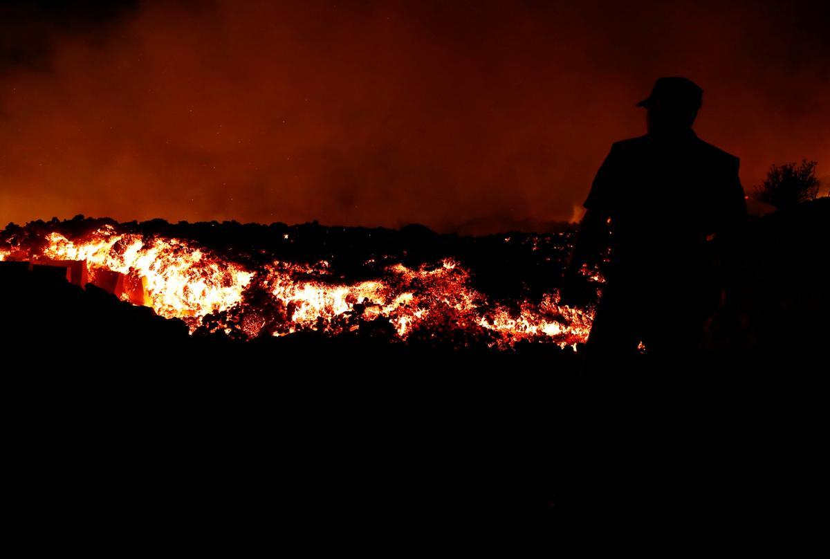 Lava flows next to a local police officer following the eruption of a volcano in Spain