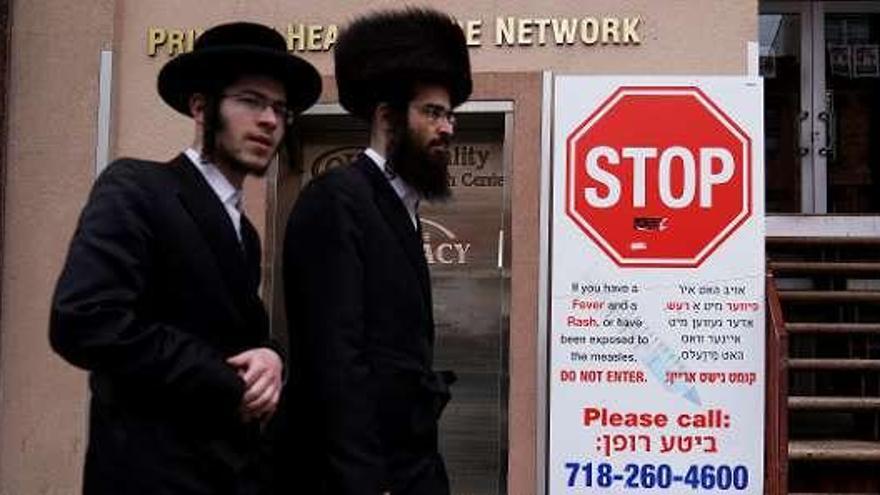 Dos judíos ortodoxos pasan frente a un cartel que prohíbe pasar a quien tenga síntomas del sarampión, en Brooklyn, Nueva York. // C.A.