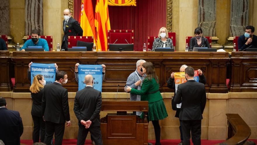 Activistas protestan en el pleno del Parlament con carteles críticos con los diputados