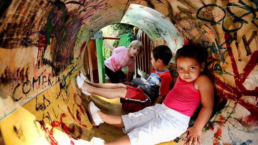 Unos niños juegan dentro de un tobogán lleno de pintadas y desperfectos.