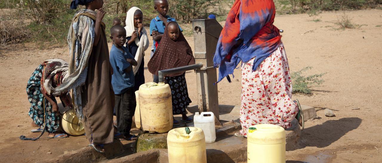 Una mujer y varios niños recogen agua en Kenia.