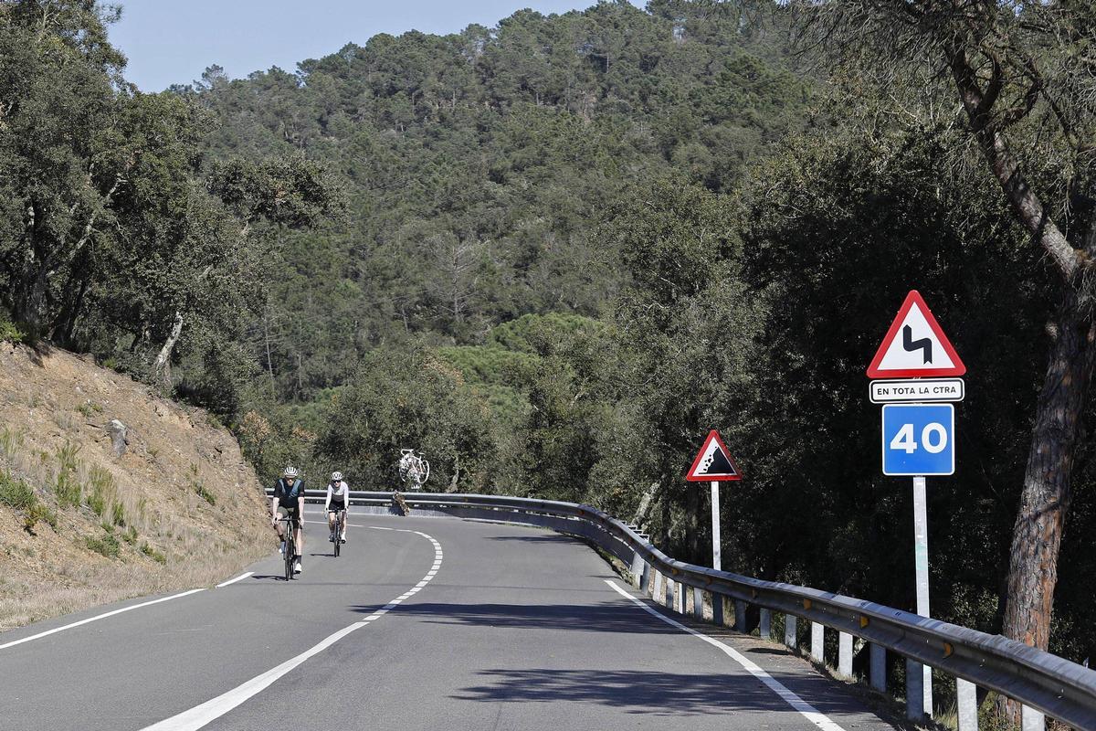 Dos ciclistes baixant i passant per davant de la bicicleta blanca  en record de Tina Vilanova.