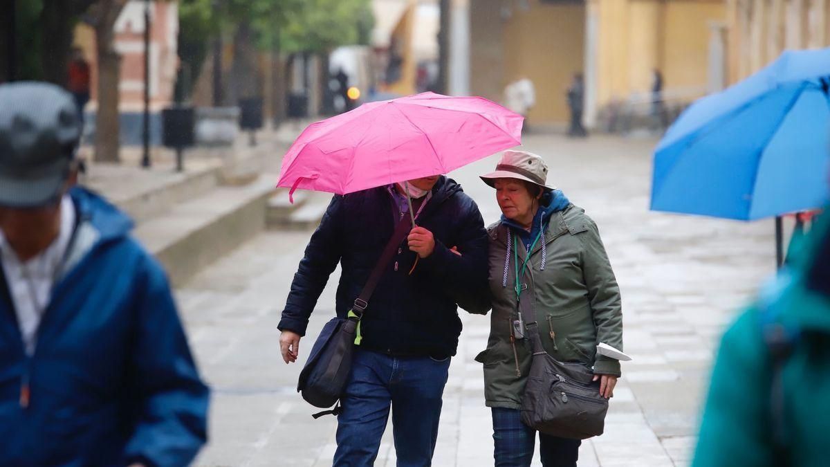 Una pareja de turistas se protege de la lluvia, este viernes, en el Patio de los Naranjos de la Mezquita-Catedral de Córdoba.