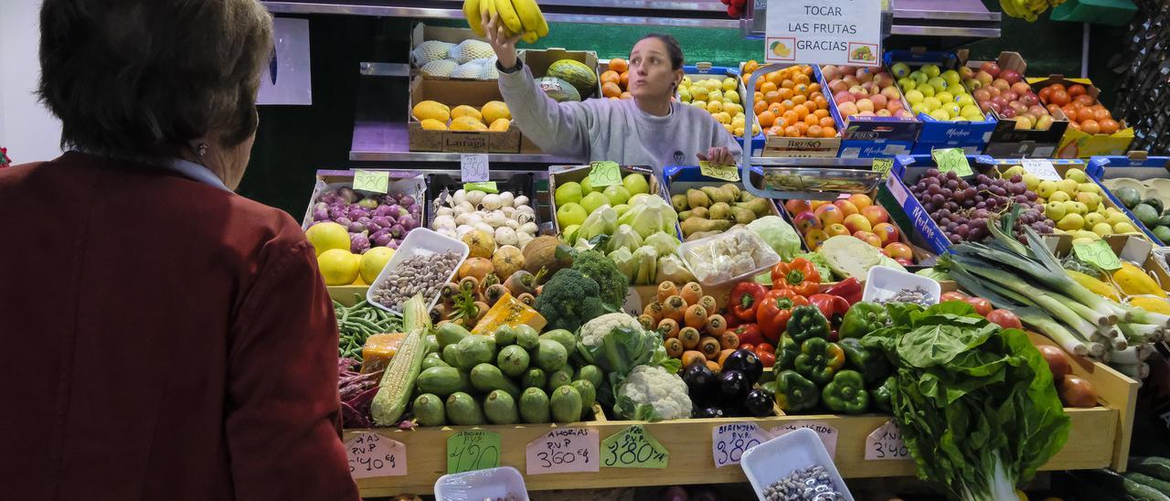 Una mujer es atendida por la tendera en un puesto de frutas y verduras.