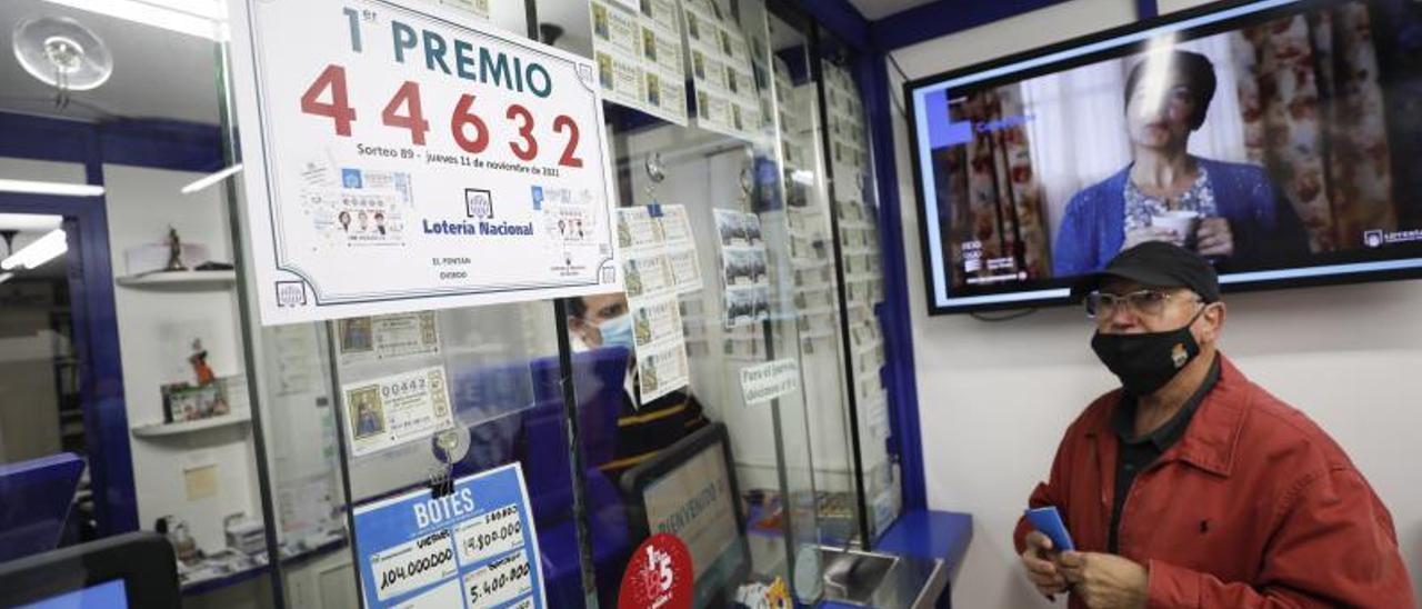 Arriba, el cliente Jesús Fernández mirando el cartel con el número agraciado en la administración. Sobre estas  líneas, los loteros Luis Manuel Gutiérrez y Ana Valdés posando con los carteles del premio. | Luisma Murias