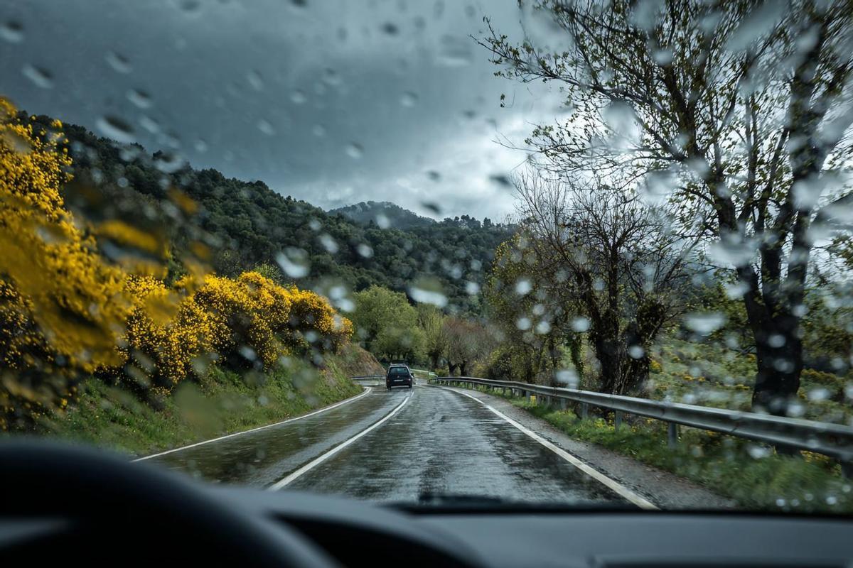 Parabrisas con gotas de agua y la carretera mojada de la lluvia