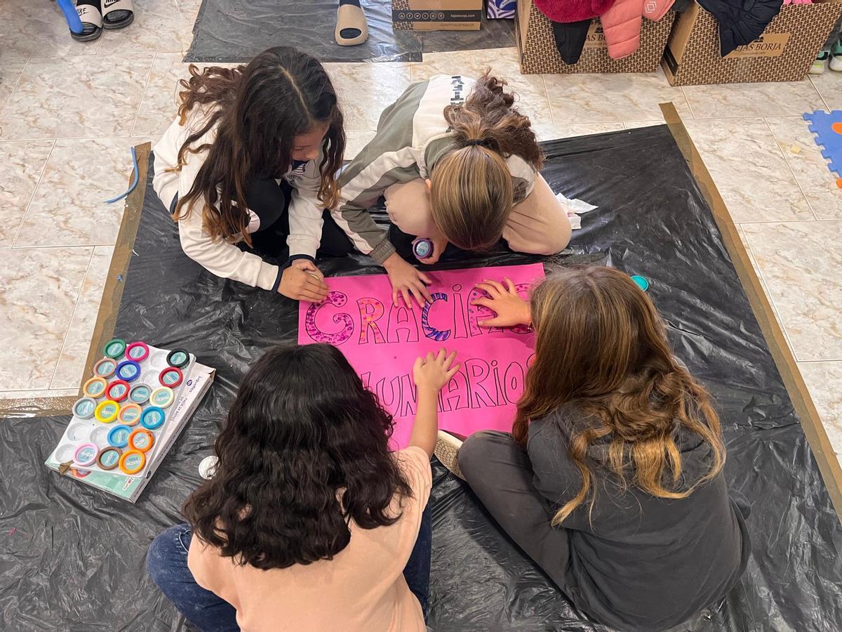 Un grupo de niñas pinta una pancarta de agradecimiento a los voluntarios.