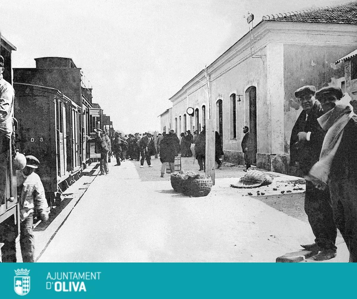 Varias personas en la estación de Oliva con un tren parado en la vía.