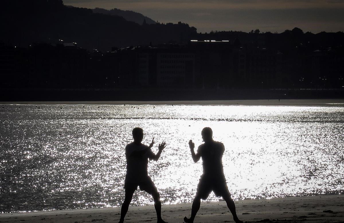 Dos hombres practican artes marciales al amanecer en la playa de Ondarreta de San Sebastián, donde este jueves los cielos se presentan con intervalos de nubes medias y altas que aumentarán al final del día hasta quedar cubiertos con lluvias y chubascos por la noche.