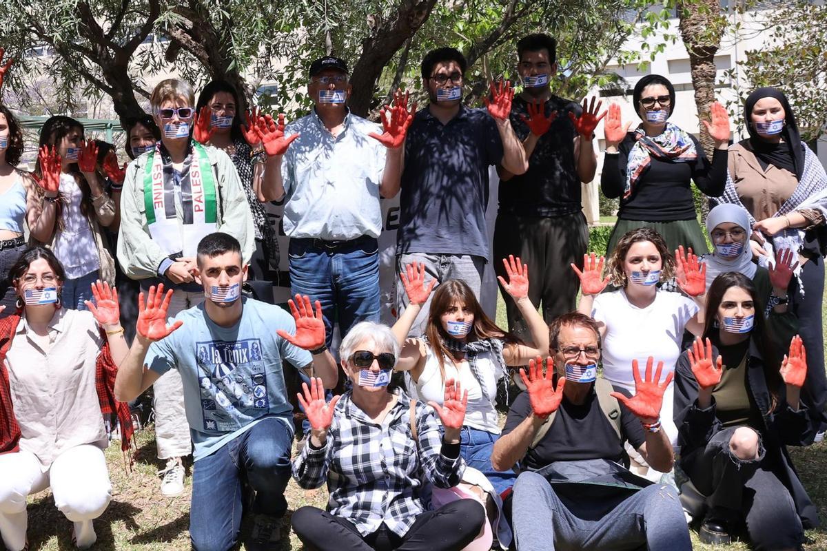 Asistentes a la acampada de la UA con las manos rojas y banderas de Estados Unidos e Israel cubriendo sus bocas