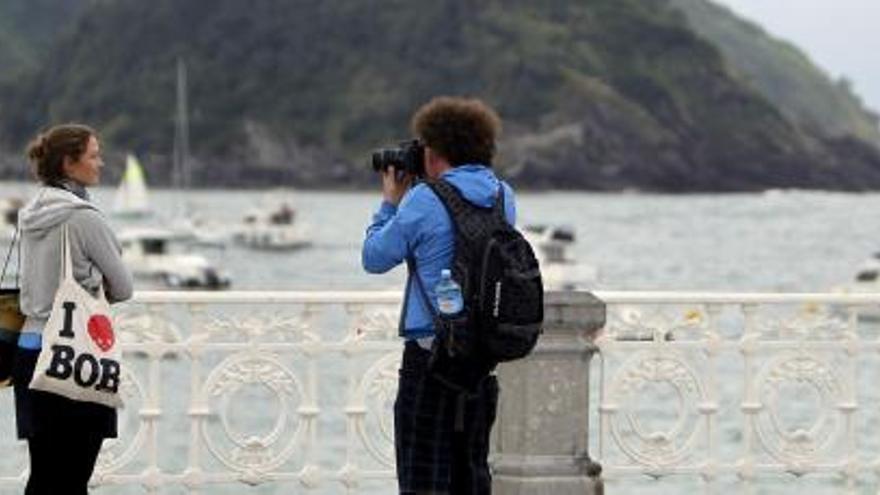 dos turistas se fotografían junto a la playa de La Concha.
